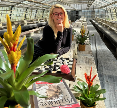 Caroline Uhl, lächelnd an einem Tisch im Gewächshaus